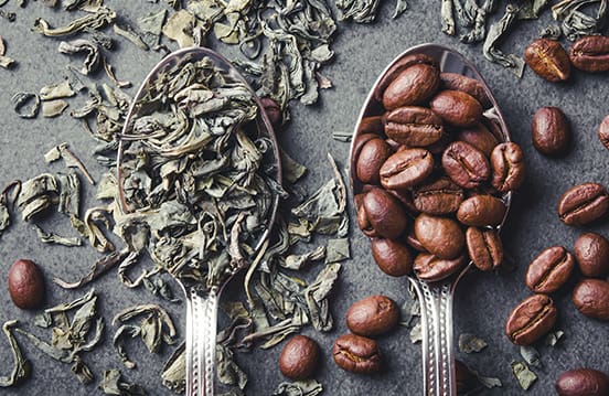 Green tea leaves and coffee seeds on metal spoons.